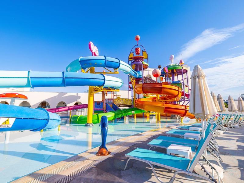 Bunter Wasserpark mit Rutschen und Liegestühlen unter blauem Himmel.
