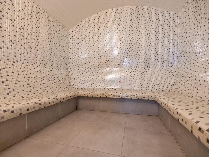 Innenraum eines Dampfbads mit gewölbten Wänden und Sitzbank aus Mosaikfliesen.