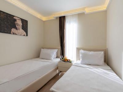 Licht ingericht hotelkamer met twee eenpersoonsbedden, wit beddengoed en een raam met gordijn.