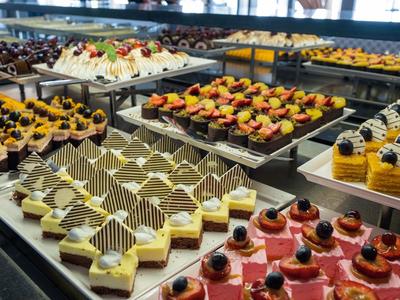 Vielfältige bunte Desserts mit Schokolade, Früchten und Sahne auf Tabletts in einer Vitrine.