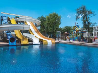 Wasserpark mit großen, bunten Wasserrutschen über blauem Pool und umgeben von Bäumen.
