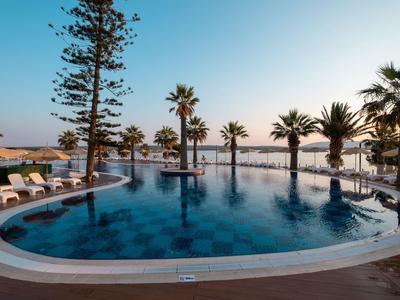 Round pool with palm trees and lounge chairs by the sea at sunset.