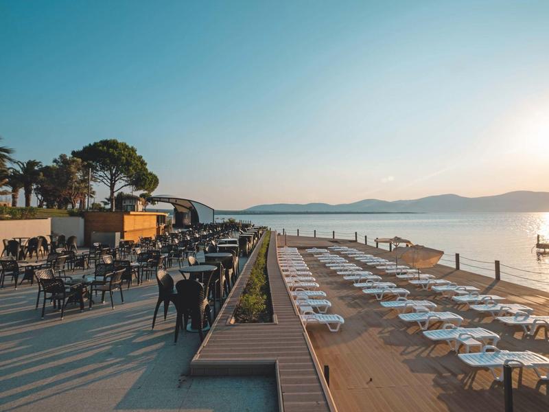 Pohled za západu slunce na plážovou jídelní zónu a lehátka na dřevěném mole u vody.