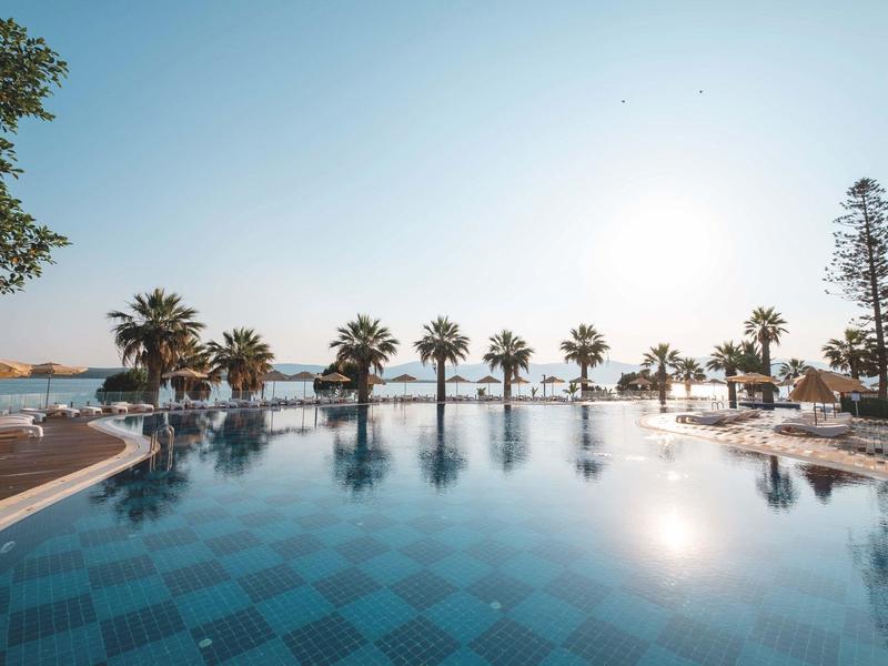 Jasná obloha u bazénu v resortu s palmami podél okraje při západu slunce.