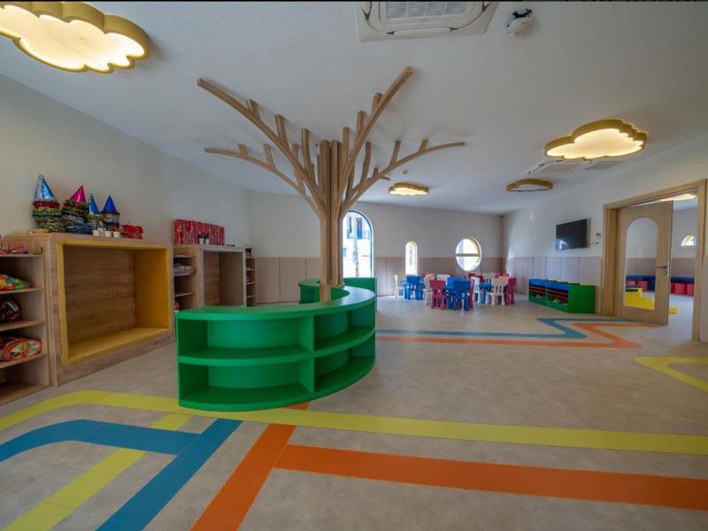 Barevná herna s policí ve tvaru stromu a stoly v pozadí