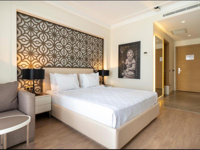 Moderní hotelový pokoj s manželskou postelí, vzorovaným čelem postele a nočními stolky s lampami.