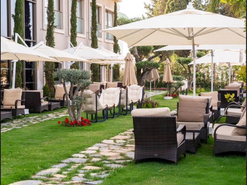 Venkovní terasa s proutěnými židlemi a slunečníky na zeleném trávníku vedle hotelové budovy.