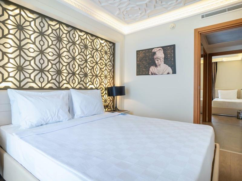 Světý hotelový pokoj s velkou postelí, vzorovanými žaluziemi a uměleckým dílem na stěně.