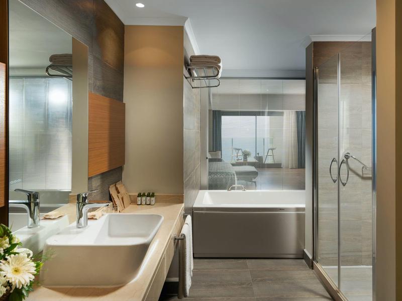 Modern bathroom with double sinks, bathtub, glass shower, and beige tile decor.