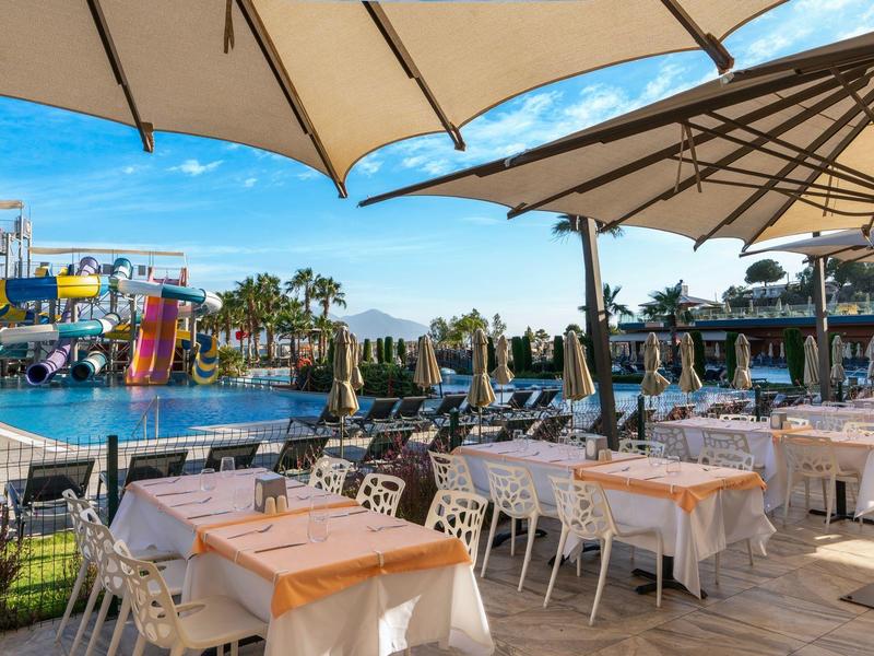 Outdoor dining area with tables, umbrellas, and a colorful water park in the background.