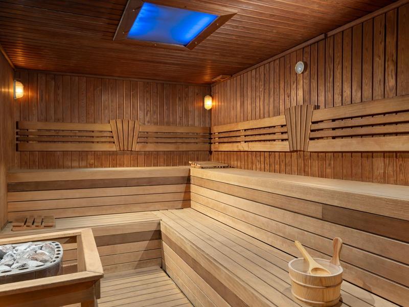Wood-paneled sauna with tiered wooden benches, a bucket, and warm lighting.
