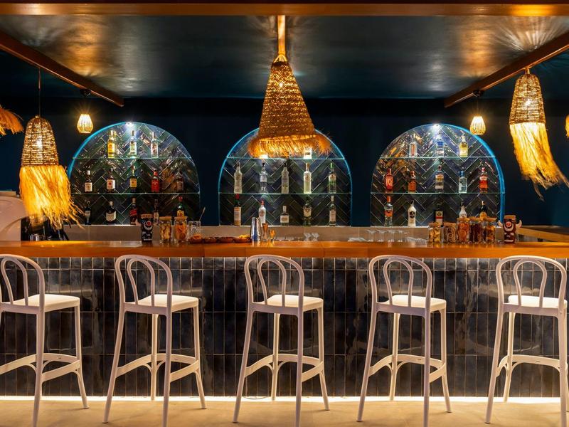 Cozy bar with wooden stools, warm lighting, and decorative hanging lamps in a dark ceiling setting.