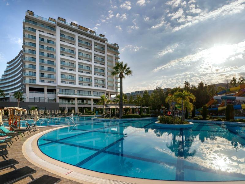 Hotel with large outdoor pool, lounge chairs, and palm trees under a partly cloudy sky.