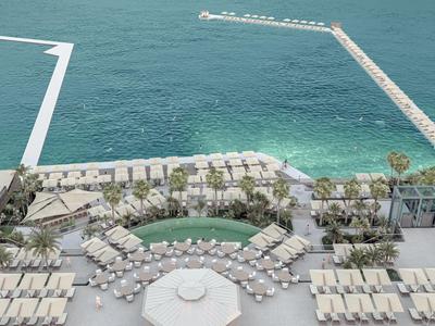 Vista di un resort sulla spiaggia di lusso con sdraio, palme e piscina vicino al mare.