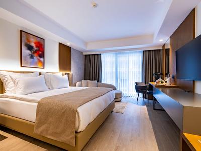 Camera d'hotel moderna con letto matrimoniale, scrivania e finestra grande con tende.