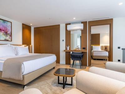 Camera d'hotel moderna con letto matrimoniale, poltrone comode e specchi alle pareti in tonalità neutre.