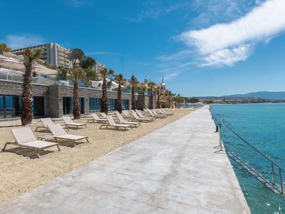 Ampia spiaggia sabbiosa con lettini e palme accanto a un mare azzurro e edifici alberghieri.