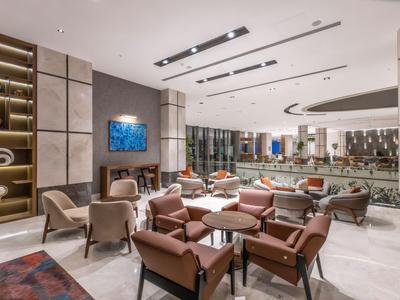Lounge dell'hotel moderno con comode poltrone, tavoli in vetro e illuminazione elegante.