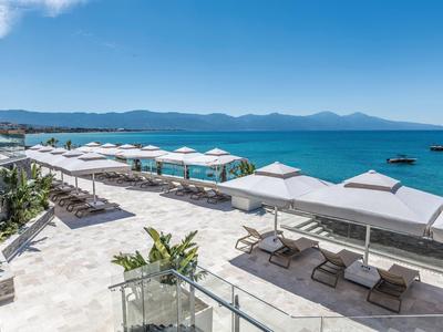 Vista di una terrazza dell'hotel con lettini e ombrelloni sul mare con le montagne sullo sfondo.