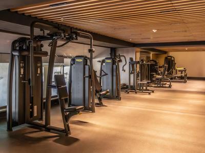 Ampia palestra moderna con diverse macchine per allenamento di forza e pavimento in legno.