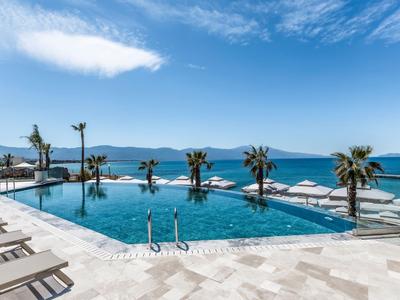 Piscina dell'hotel con sdraio e vista sul mare sotto un cielo azzurro.