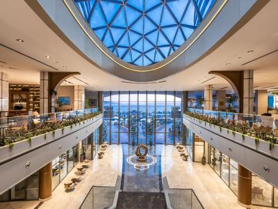 Ampia hall d'hotel con cupola di vetro, arredamento elegante e vista sull'acqua.