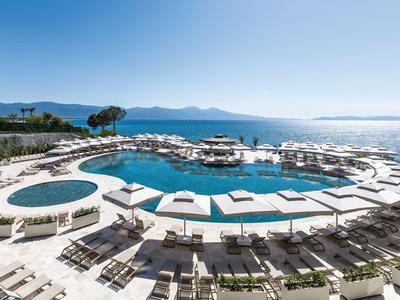 Grande piscina dell'hotel con lettini e vista sul mare in una giornata di sole.