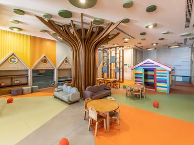 Area giochi colorata in hotel con scultura ad albero, struttura per arrampicarsi e mobili per bambini.