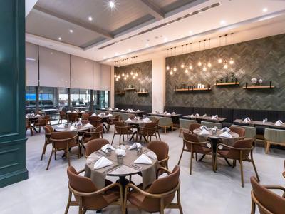 Area ristorante moderna in hotel con tavoli in legno, sedie e pareti decorative.