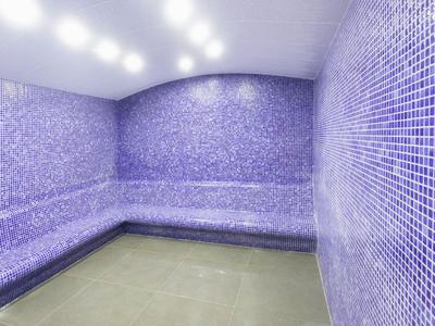 Sala sauna con piastrelle a mosaico viola su pareti e panche, illuminata.