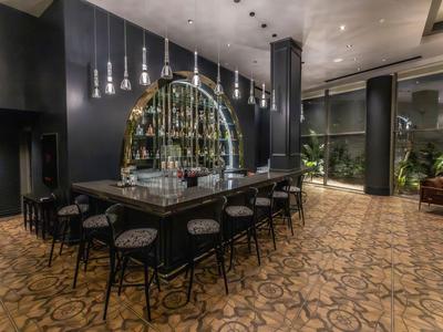 Area bar moderna di un hotel con sgabelli intorno a un banco centrale e arredamento interno scuro.