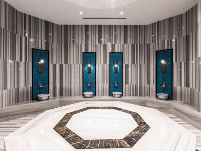 Moderno hammam turco con piattaforma centrale in marmo e fontane d'acqua verticali.