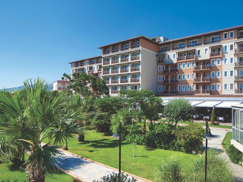 Großes Hotelgebäude mit mehreren Stockwerken, umgeben von grünen Palmen und gepflegtem Garten.