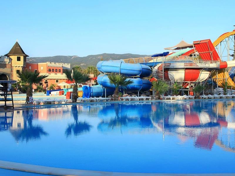 Großer Pool mit Wasserrutschen und Sonnenschirmen in sonniger Ferienanlage.