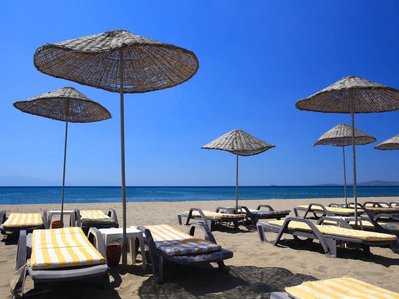 Leerer Sandstrand mit Sonnenliegen und Strohmachirmen unter klarem blauem Himmel.