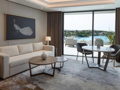 Moderner Wohnraum mit Sofa, Tisch, Kunst an der Wand und großer Glasfront mit Blick auf Wasser.