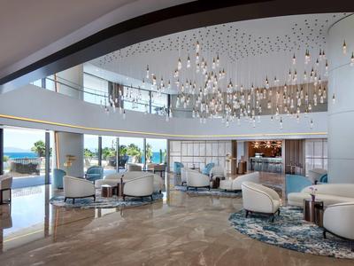 Großer, heller Lounge-Bereich mit modernen weißen Sesseln, blauen Kissen, Kronleuchtern und Meerblick.