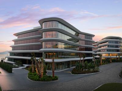 Modernes Hotelgebäude mit geschwungenen Balkonen und Glasfront bei Sonnenuntergang.