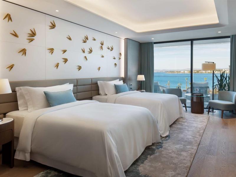 Modernes Hotelzimmer mit zwei Betten, großen Fenstern, Meeresblick und stilvoller Wanddekoration.
