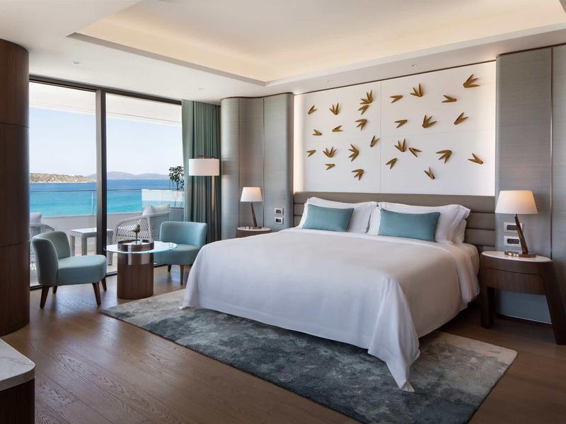 Modernes Schlafzimmer mit großem Bett, blauen Sesseln, Meerblick und Wandschmuck aus Vogelmotiven.