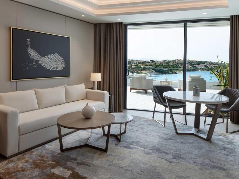 Moderner Wohnraum mit Sofa, Tisch, Kunst an der Wand und großer Glasfront mit Blick auf Wasser.