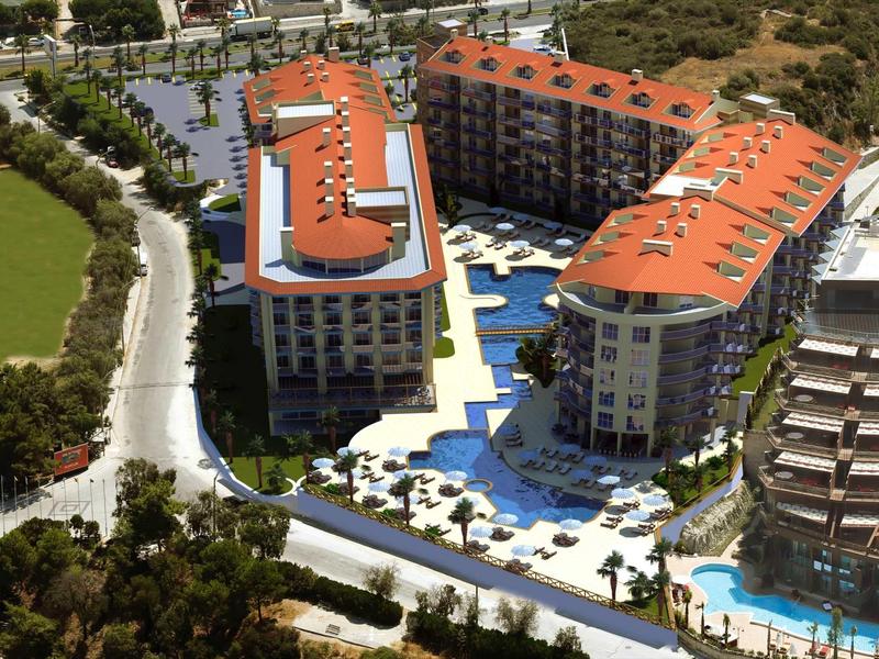 Ośrodek hotelowy z basenami i czerwonymi dachami otoczony zielenią.