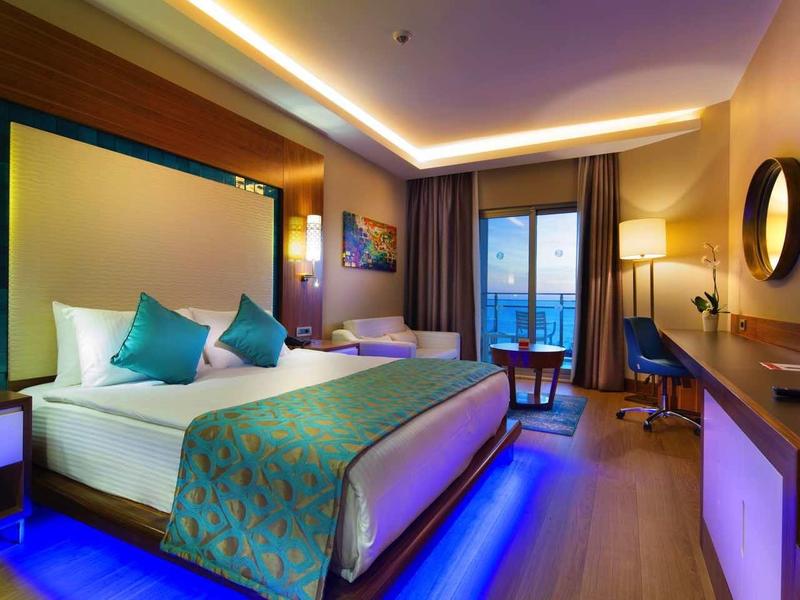 Nowoczesny pokój hotelowy z dużym łóżkiem, niebieskimi dekoracjami i balkonem z widokiem.