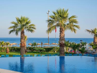 Piante di palma vicino a una piscina con ombrelloni e il mare sullo sfondo