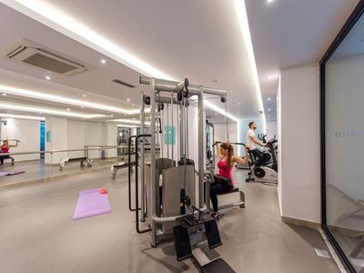 Salle de sport avec différents appareils d'exercice et grandes fenêtres donnant sur l'extérieur.