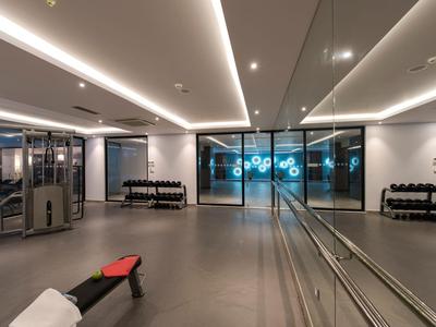 Salle de sport moderne et lumineuse avec grands miroirs, équipements de fitness et éclairage indirect au plafond.