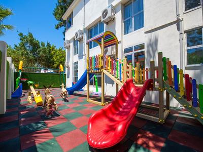 Area giochi luminosa con scivoli e strutture per arrampicarsi accanto a un edificio alberghiero.