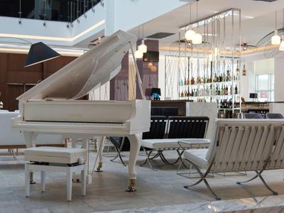 Pianoforte bianco con sgabello abbinato in lounge d'hotel moderno con area salotto e bar.