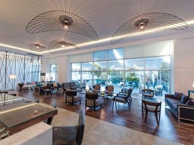 Ampia lounge dell'hotel con illuminazione moderna, aree salotto e grandi finestre con vista sul verde.