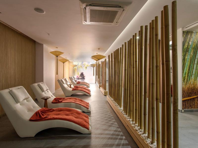 Lounge spa moderna con sedie reclinabili bianche e asciugamani arancioni accanto a separé in bambù.